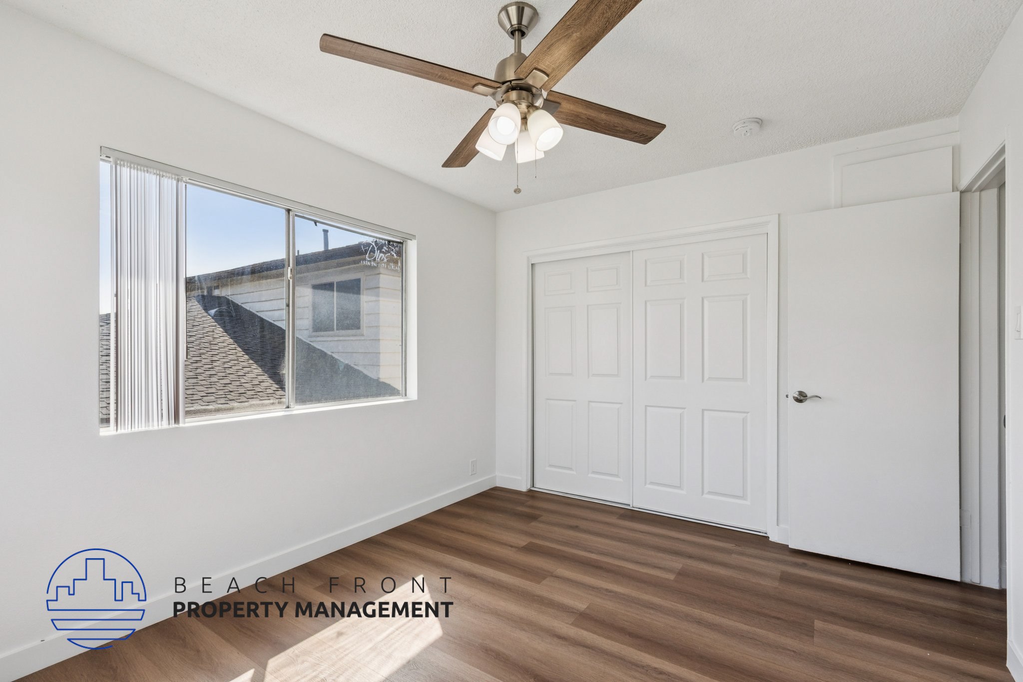 A room with a ceiling fan and a window overlooking a roof.